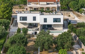 A modern two-story building with a flat roof, outdoor seating area, and a swimming pool. - Cozy home in Maslenica (Maslenica)