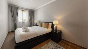 A hotel room with a bed, nightstands, a lamp, and a view of the city through the window. - Casa Filomena - Castle Walls (Óbidos)