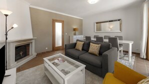 A living room with a fireplace, a sofa, a coffee table, and a dining area with chairs. - Casa Filomena - Castle Walls (Óbidos)