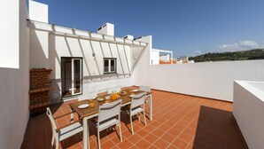 A rooftop terrace with a dining table, chairs, and a brick wall. - Casa Filomena - Castle Walls (Óbidos)