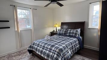 Una camera da letto con un letto, un ventilatore a soffitto, un comodino, una lampada e una finestra.