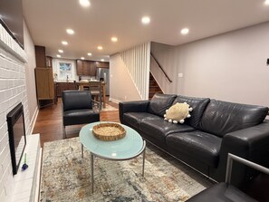 Ein Wohnzimmer mit einer schwarzen Ledersofa, einem Glastisch und einem gemusterten Teppich.