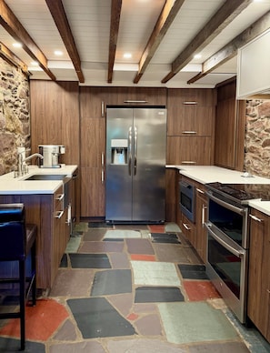 A kitchen with a stainless steel refrigerator, wooden cabinets, a stone-patterned floor, and a built-in oven. - Creekstone House • Walk to Town • Hot Tub + Parking (New Hope)
