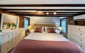 Un dormitorio con una cama grande, vigas de madera, pared de ladrillo y un aparador blanco.