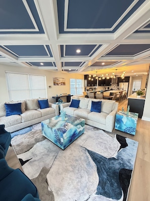 A modern living room with a sectional sofa, a coffee table with a blue abstract design, and a large rug. - Brand New Custom Furnished 4-Bedroom House in Ventnor/Bay Views & Walk to Beach (Ventnor City)