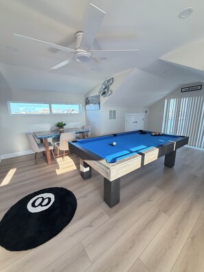 A modern room with a pool table, ceiling fan, and a sign indicating a game room.