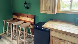 A compact kitchen with wooden stools, a black dishwasher, and a window with a view. - Cozy Off Grid Cabin on the Prairie perfect for your getaway to Montana (Billings)