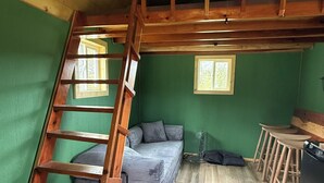 Een loft-achtige kamer met een houten ladder, een bank, een eettafel en een kroonluchter.