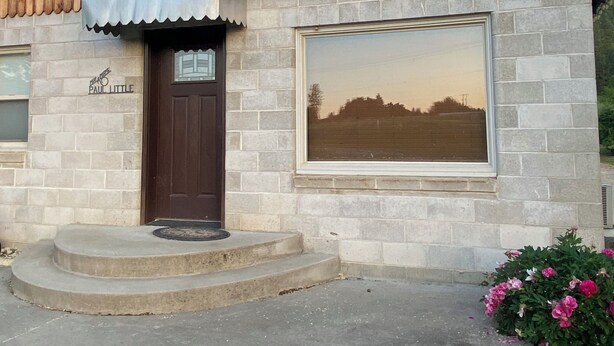 A rustic building with a wooden facade, a stone wall, a large window, and a door with a sign above it.