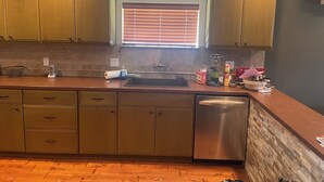 A kitchen with wooden cabinets, a stainless steel dishwasher, and a window with blinds.