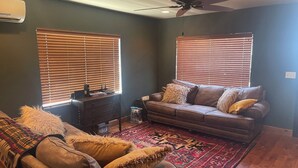 A living room with a brown leather sofa, a patterned rug, and a ceiling fan.
