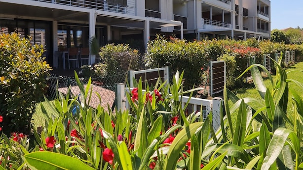 A multi-story hotel with balconies, a garden with various plants, and a clear sky. - Marina Apartment With Terrace (Mandelieu-La-Napoule)