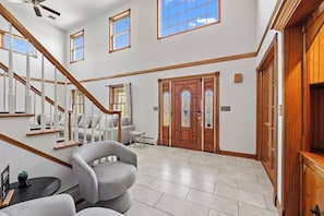A spacious interior with a staircase, a wooden door with glass panels, and a seating area with a chair and a small table. - Hudson Retreat, Pool, Spa, Game Room, Gym (Gardiner)