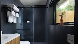 Et moderne badeværelse med en glasbrusekabine, et hvidt toilet og en trækommode.