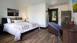 Et hotelværelse med seng, skrivebord, stol, lampe, et billede og en dør til en balkon.