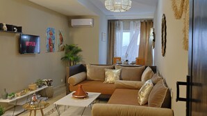 A living room with a sofa, a TV, a table with a vase, and a ceiling light. - Appartement Moderne au Centre-Ville Guéliz (Marrakech)