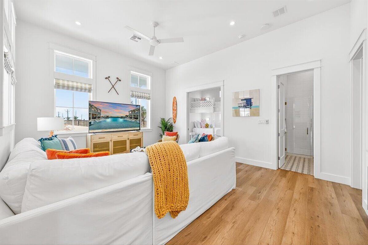 A modern living room with a white sofa, a television, and a painting of a beach scene.