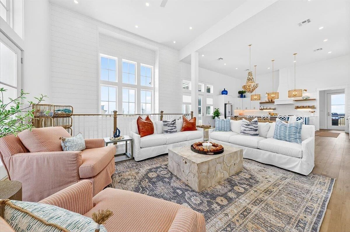 A spacious living room with large windows, a white sofa set, a coffee table, and a hanging chandelier.