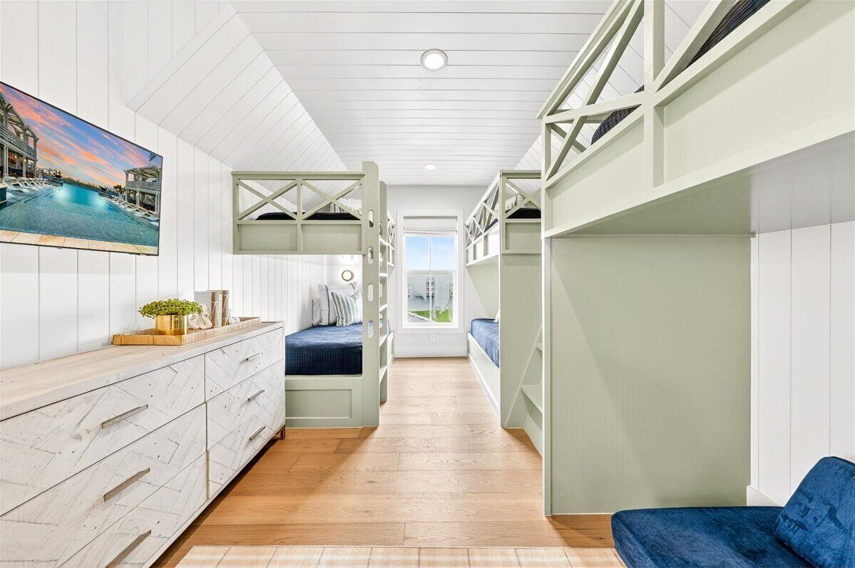 A narrow hallway with bunk beds, a wooden dresser, and a large window at the end.