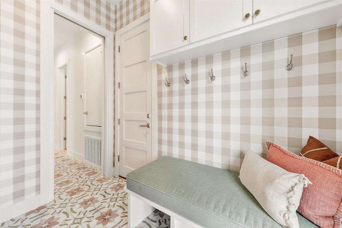 A hallway with checkered wallpaper, a bench with pillows, and a door leading to another room.