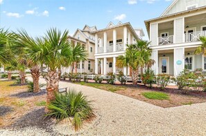 Ein Strandhotel mit überdachtem Gang, Palmen und einem Kiesweg.
