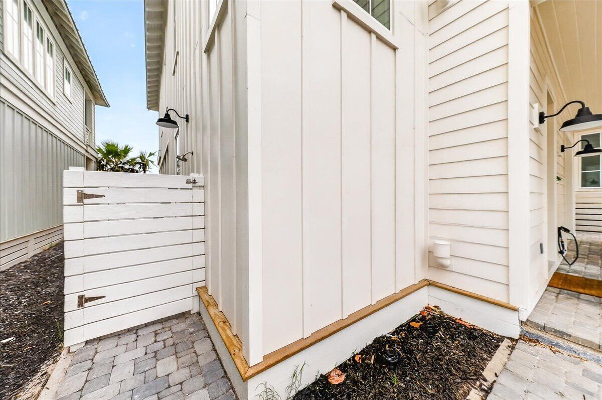 A white wooden fence with a gate, a brick pathway, and a small garden area with mulch.