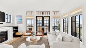 A spacious living room with a fireplace, comfortable seating, large windows, and a view of the city. - The Little Dipper - 100 STL (Port Aransas)