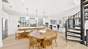 A modern kitchen with a central island, wooden chairs, pendant lights, and a spiral staircase. - The Little Dipper - 100 STL (Port Aransas)