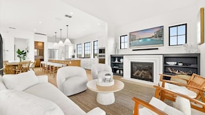 A spacious living room with a fireplace, a dining area, and a kitchen in the background. - The Little Dipper - 100 STL (Port Aransas)