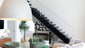 Uma sala de estar moderna com escada, móveis verdes e brancos e uma luminária pendente grande.