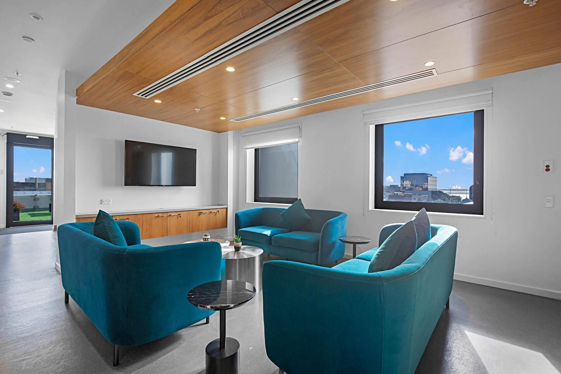 Una sala de estar moderna con sofás color turquesa, un televisor de pantalla plana y grandes ventanas con vistas a la ciudad.