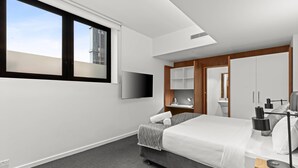 A modern hotel room with a large bed, a flat-screen TV, a desk with a lamp, and a bathroom with a mirror and sink.