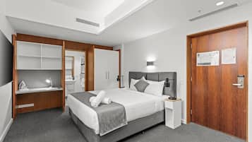 A modern hotel room with a large bed, a desk, a vanity, and a wardrobe.