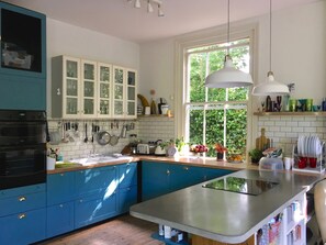 A kitchen with a large island, blue cabinets, white backsplash, and a window with greenery outside. - Large Victorian house in Crystal Palace, London (London)