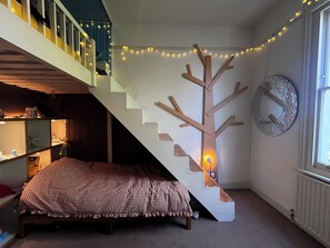 A bedroom with a bed, a staircase, a wall clock, and string lights. - Large Victorian house in Crystal Palace, London (London)