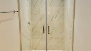 A glass-enclosed shower area with marble tiles and two metallic handles. - Suite 02 • Spacious Suite • Boutique Mansion (Guayaquil)