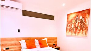 A hotel room with a bed, wooden headboard, two nightstands, a wall-mounted air conditioner, and a painting. - Suite 02 • Spacious Suite • Boutique Mansion (Guayaquil)