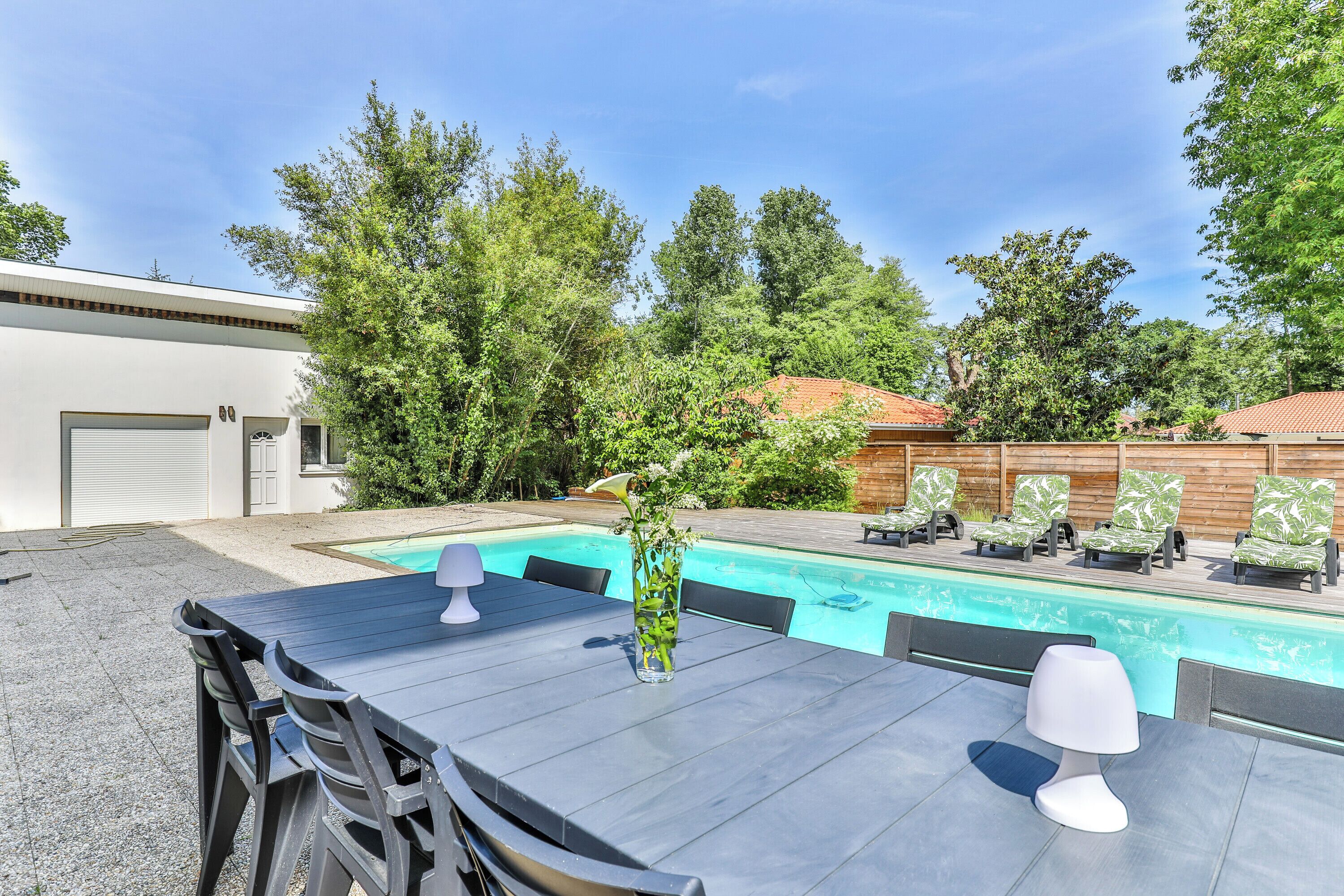 A poolside area with a table, chairs, a lamp, and lounge chairs.