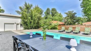 A poolside area with a table, chairs, a lamp, and lounge chairs.
