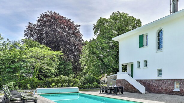 A swimming pool with lounge chairs, a patio area, and a white building with a stone foundation. - Lavignottes - AC - Piscine & Tennis (Labouheyre)