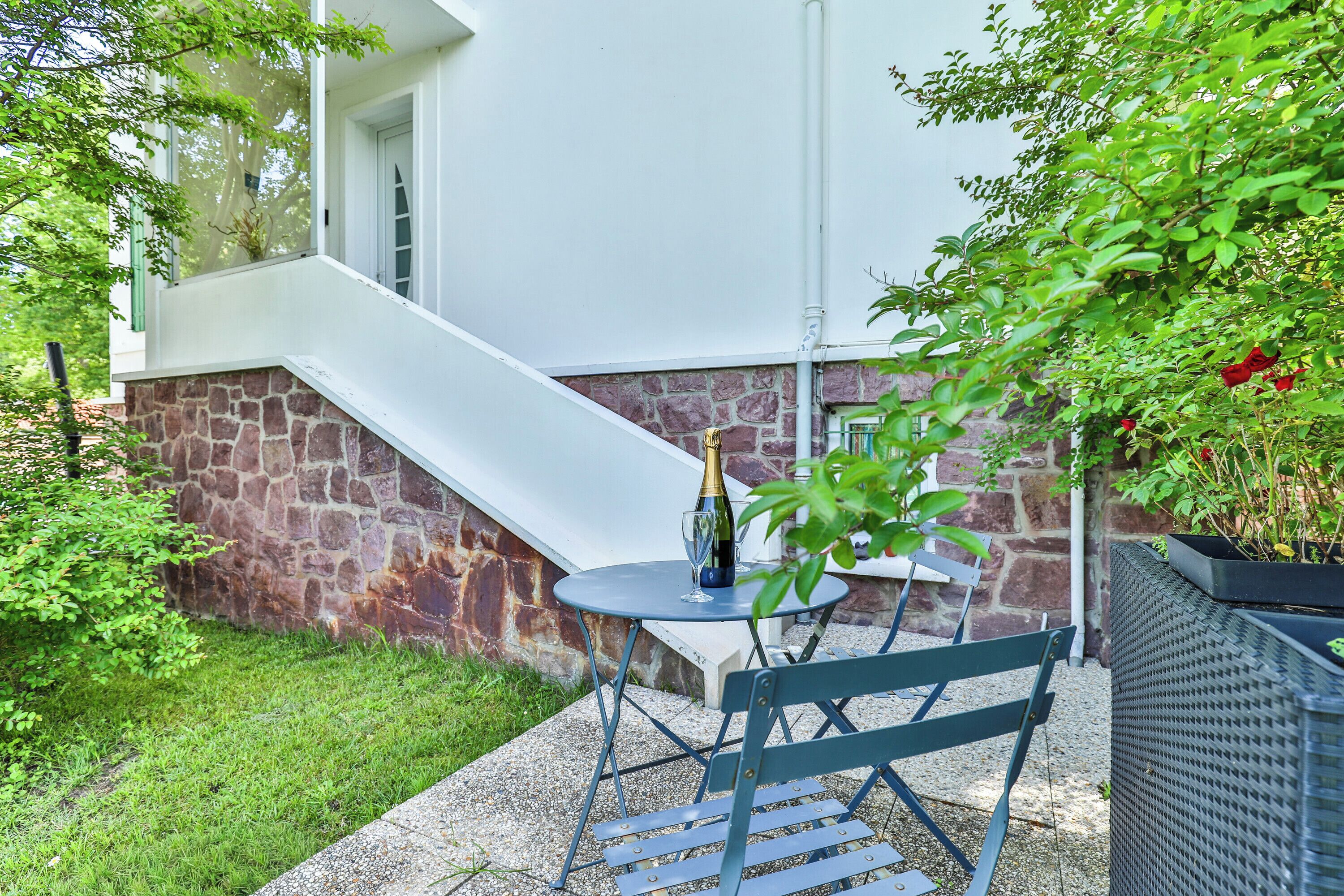 A patio with a table and chairs, a bottle of champagne, and a stone wall.