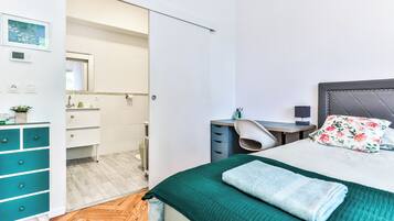 A bedroom with a bed, a desk, a chair, a wardrobe, and a bathroom visible through an open door.