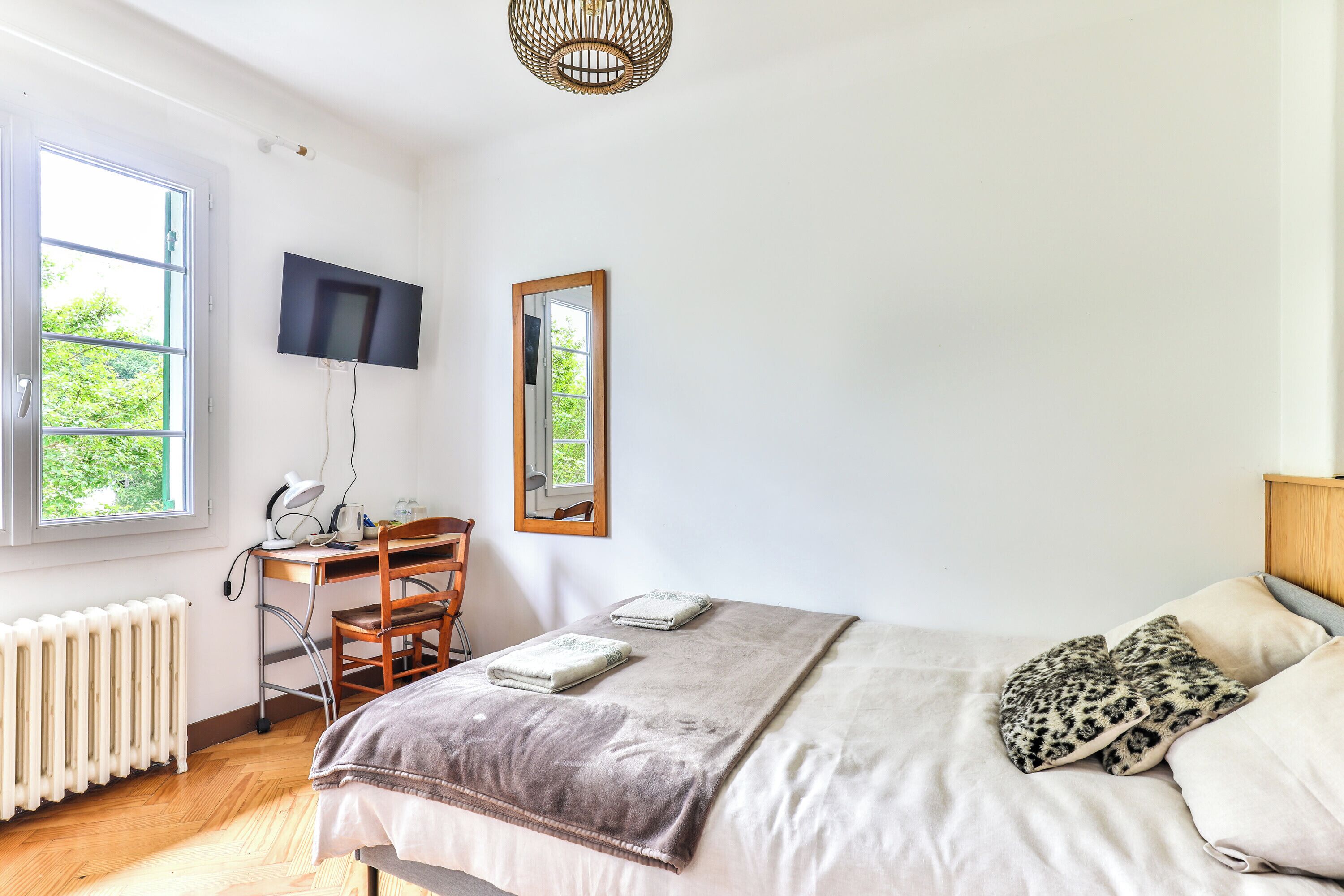 A bedroom with a bed, a desk, a chair, a TV, and a window.