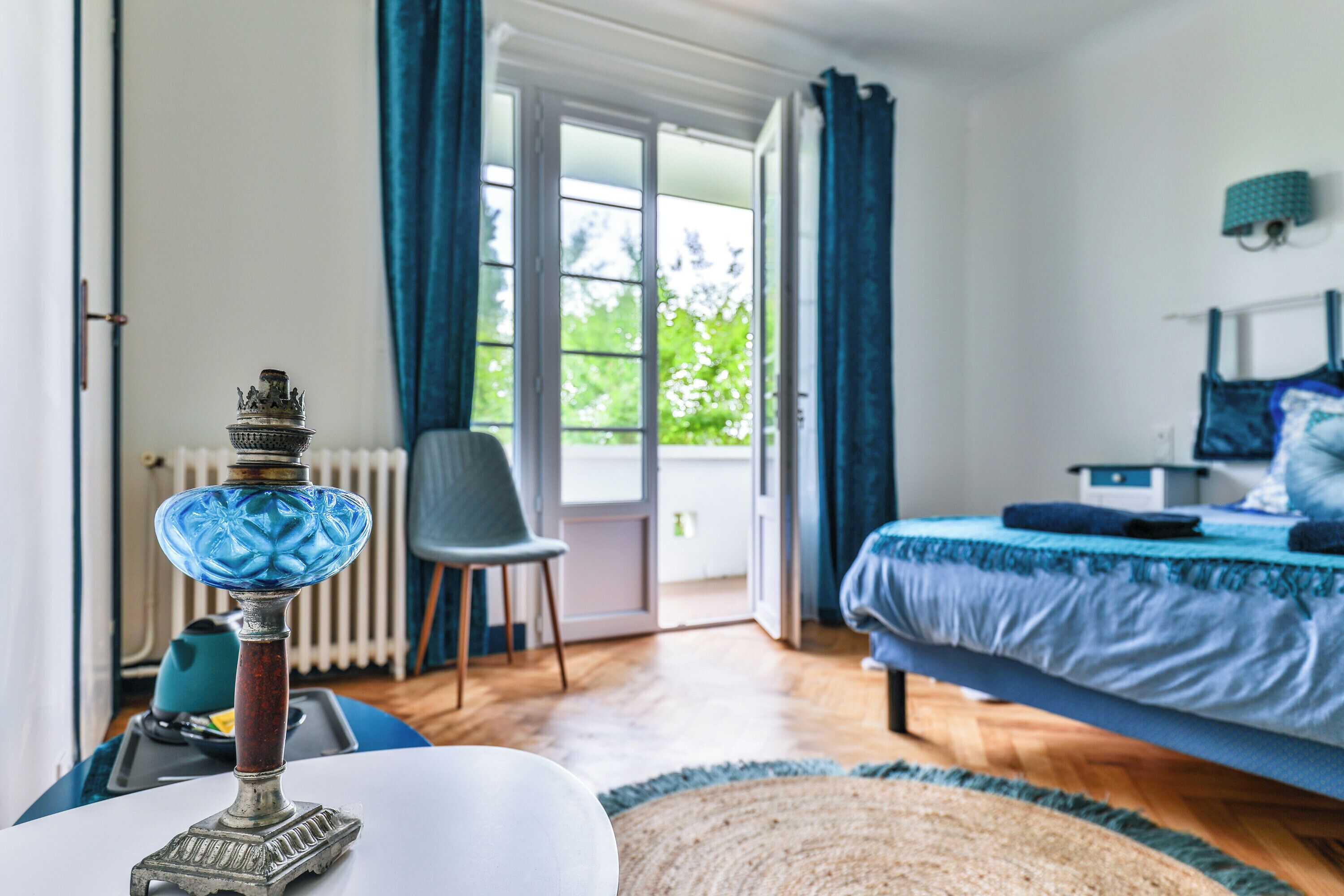 A bedroom with a bed, a chair, a table with a lamp, and a view of the outdoors through a door.