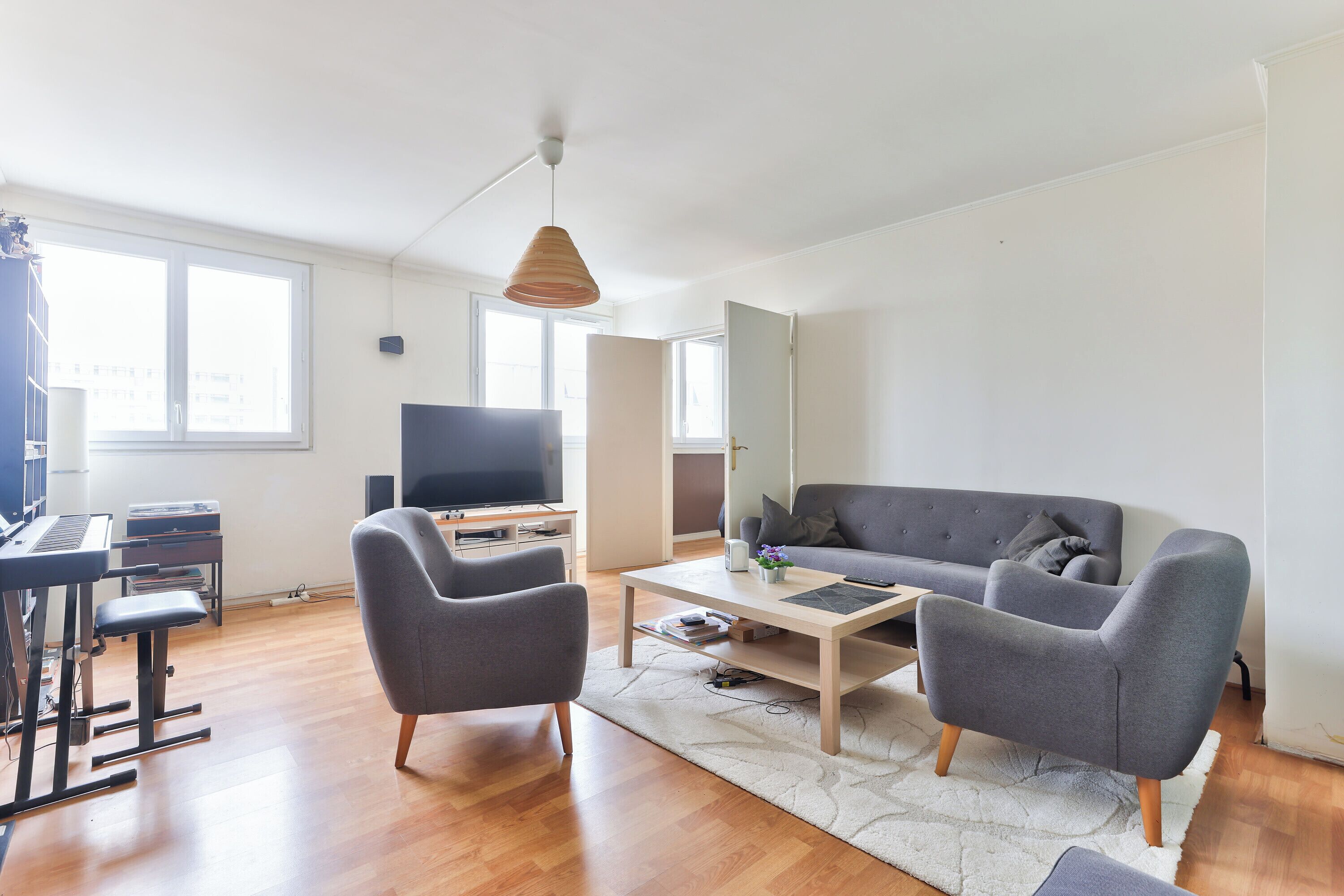 En moderne stue med sofa, lænestole, sofabord, fjernsyn og et klaver.