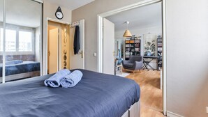 Ein Schlafzimmer mit Bett, einer Uhr und Blick auf eine Stadtansicht durch ein Fenster.