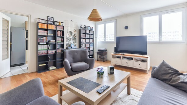 Ein modernes Wohnzimmer mit einer Couch, einem Couchtisch, einem Bücherregal, einem Fernseher und einem großen Fenster.