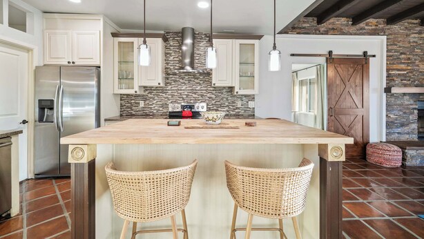 A kitchen with a central island, stainless steel refrigerator, and hanging pendant lights.