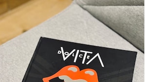 Musta esine, jossa on valkoista tekstiä ja oranssi kuvio harmaalla kangaspinnalla.
