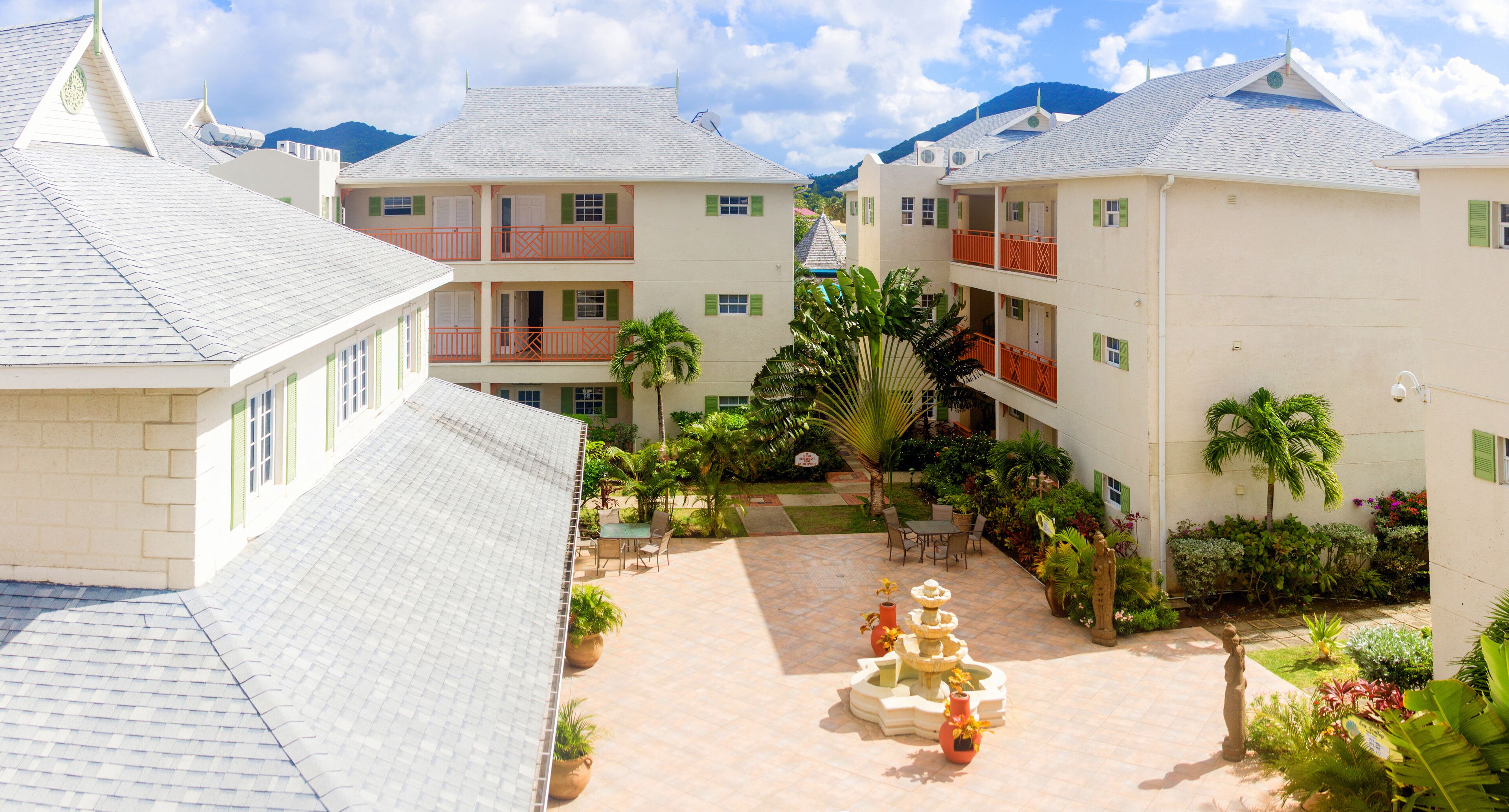 A hotel courtyard with a central fountain, multiple balconies, and lush greenery.